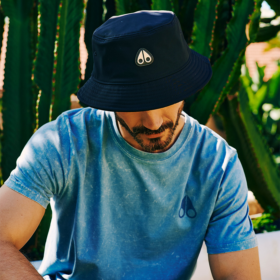 A man wearing a blue T shirt and a bucket hat sitting in the sun