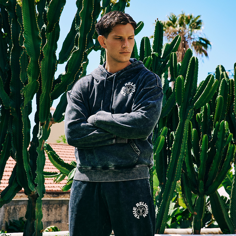 A man wearing a True Religion tracksuit standing by some cacti