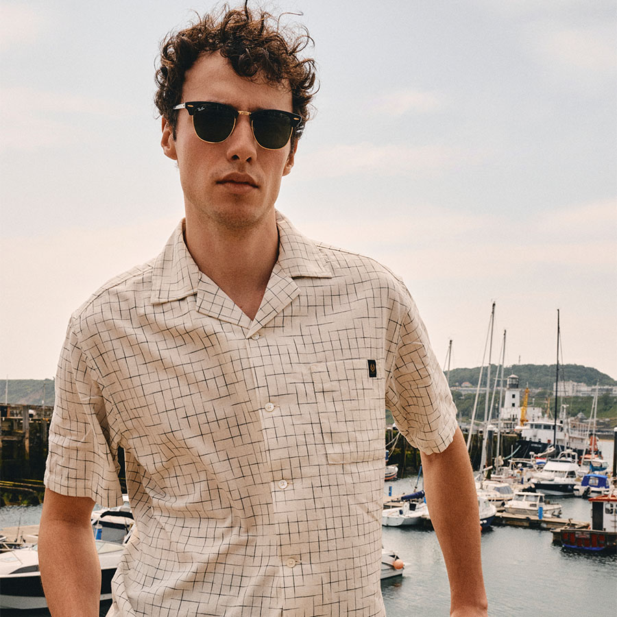 A man wearing a Belstaff shirt in front of a harbour 